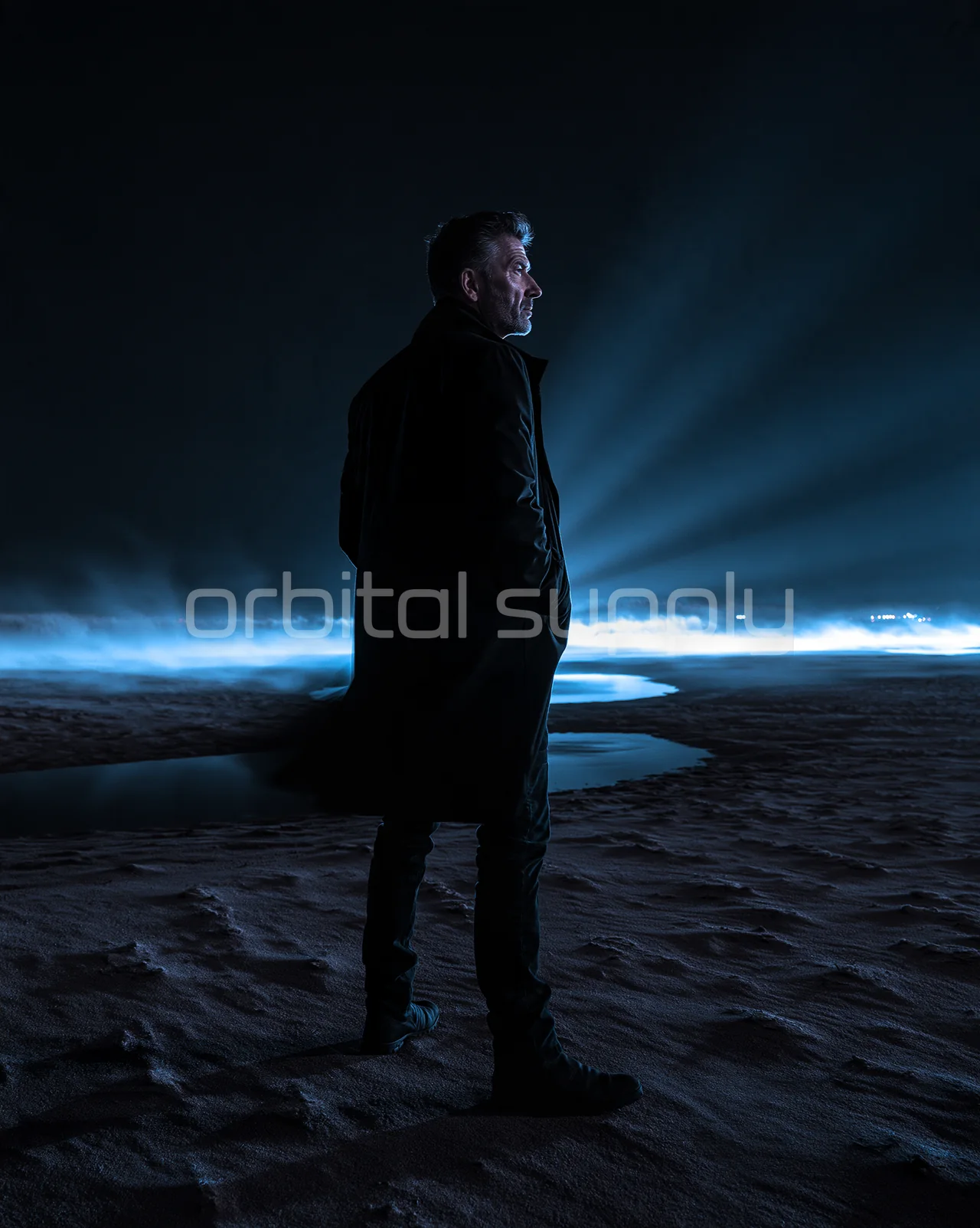 A solitary person in a dark coat stands beside pools of water and low blue mist.