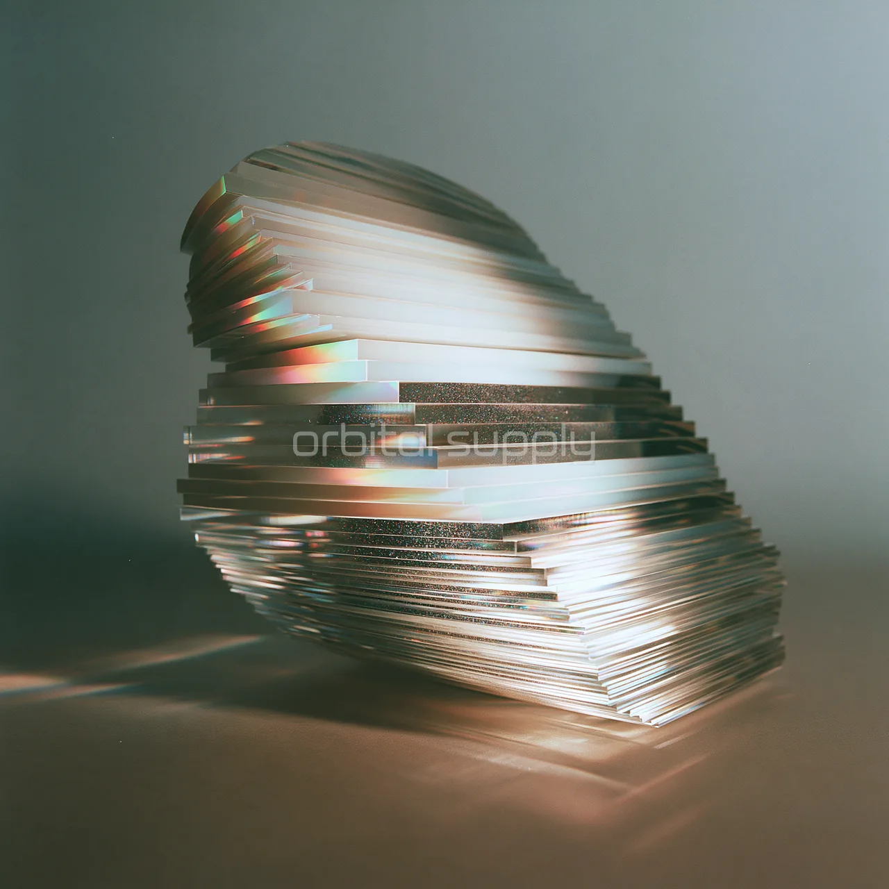 A layered sculptural object of horizontal opalescent fragments rests on a muted studio surface.