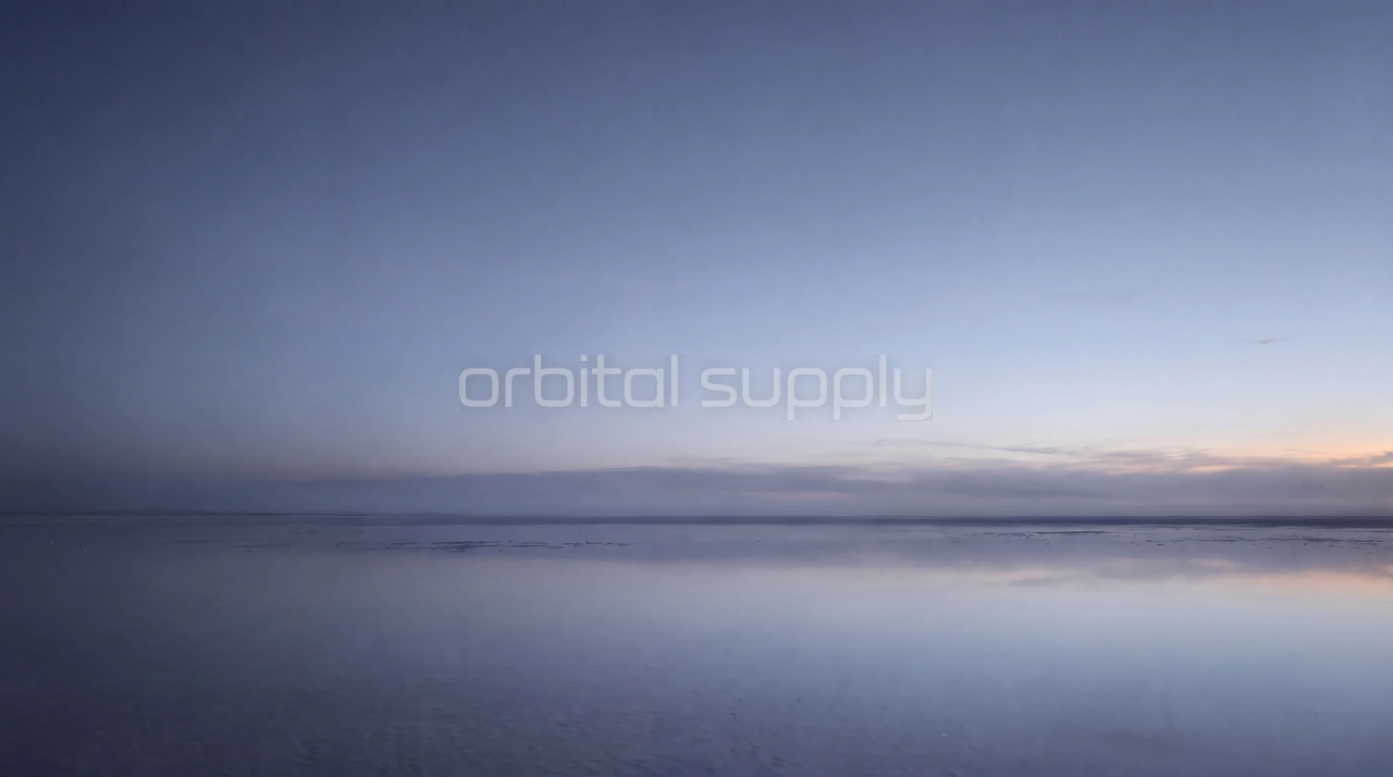 An empty salt flat mirrors a calm blue-hour sky with a faint warm glow on the horizon.