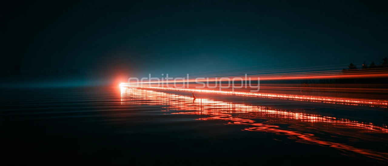 A long trail of coral light glides low over still black water toward a distant shore.