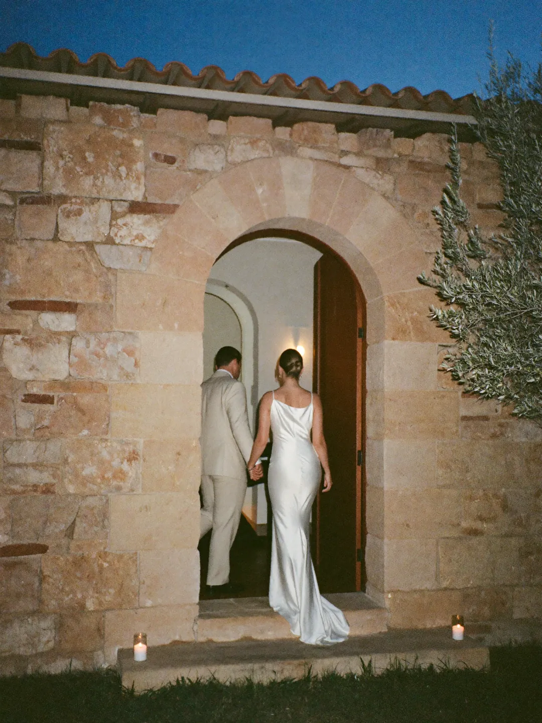 A couple walking into the house through the arched door at dusk